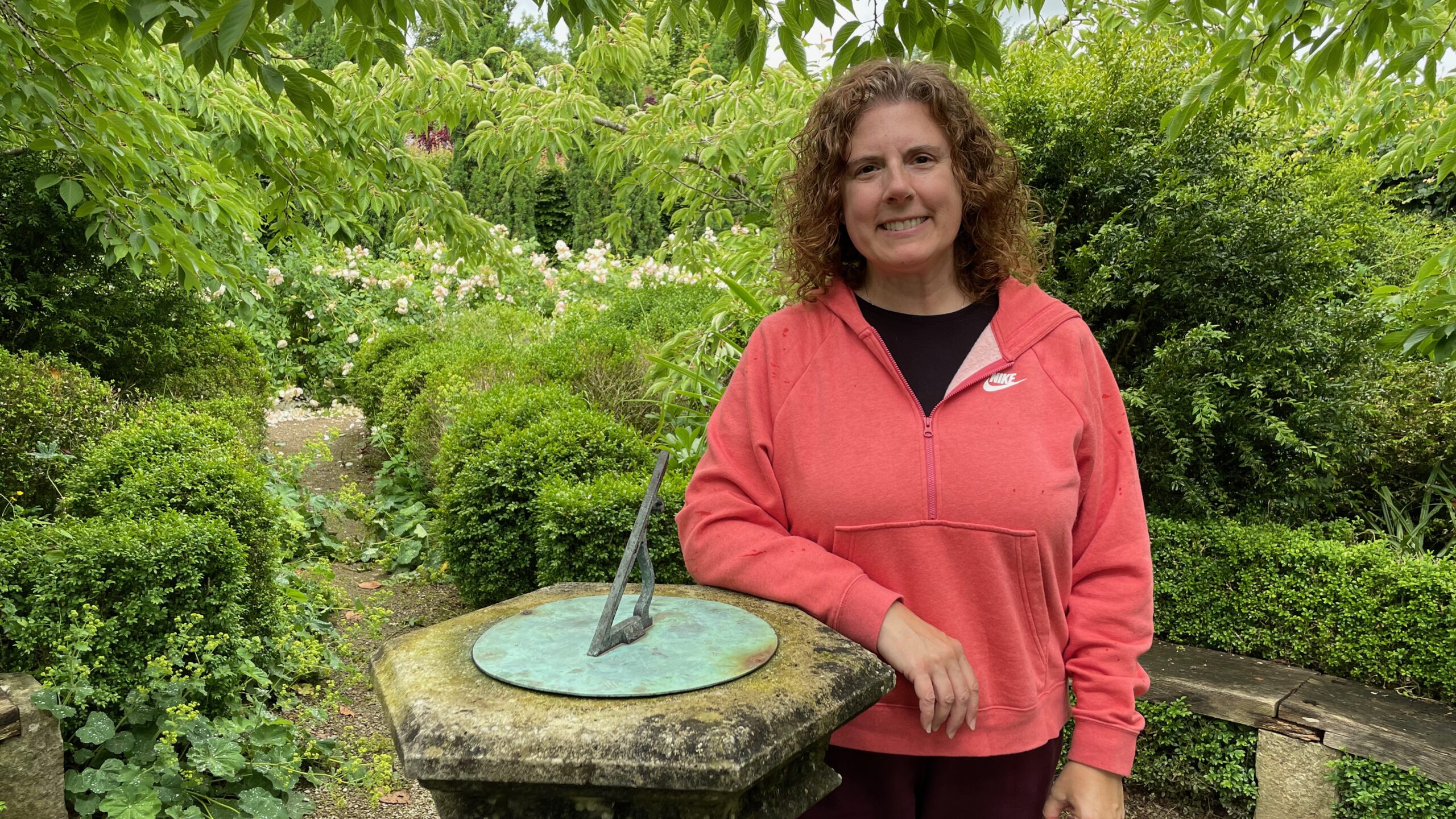 Heather wearing a red hoodie beside a garden sundial.
