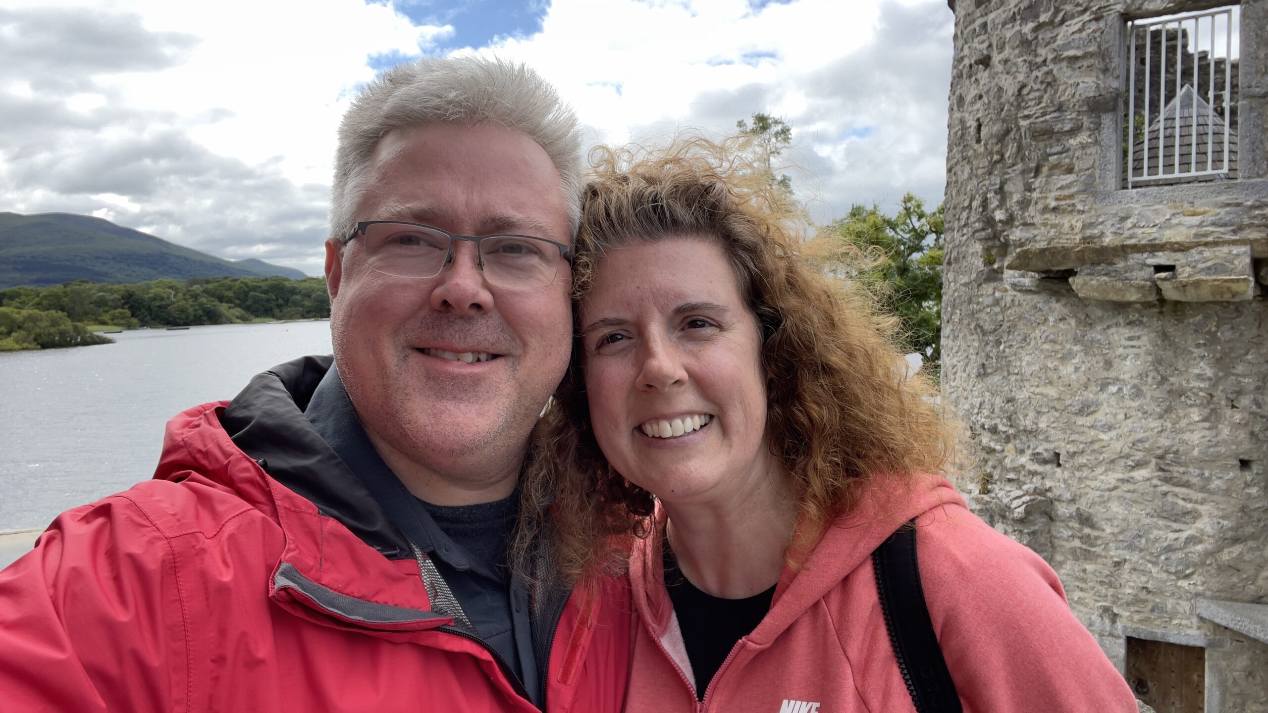 Shawn and Heather smiling together beside a lake, with a castle in the background.
